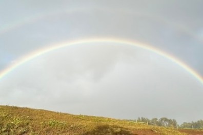 Double rainbow over a grassy hill under a cloudy sky.