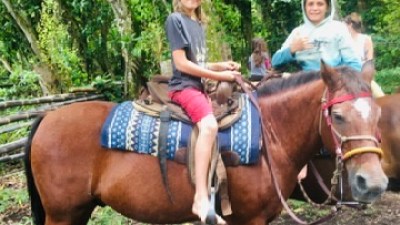 Child and adult on a horse in a forest setting.