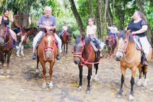 Group of people riding horses in a forested area.