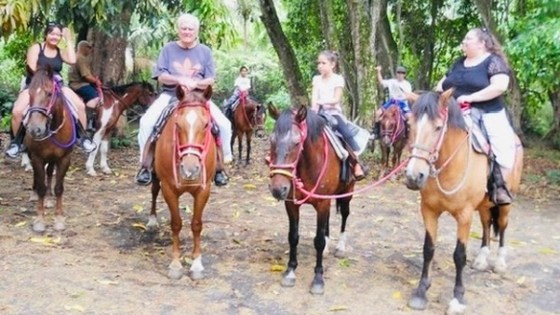 Group of people riding horses in a forested area.